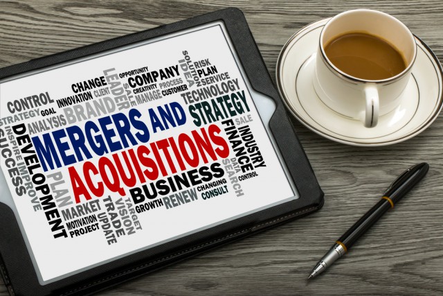 Mergers and acquisitions message displayed on a tablet, with a coffee cup and pen nearby