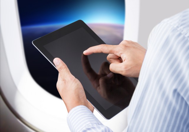 Man holding an iPad tablet on a plane next to the window