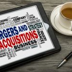 Mergers and acquisitions message displayed on a tablet, with a coffee cup and pen nearby