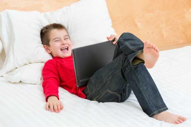 Boy laughing bed tablet laptop