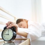 Women hitting snooze button on alarm clock