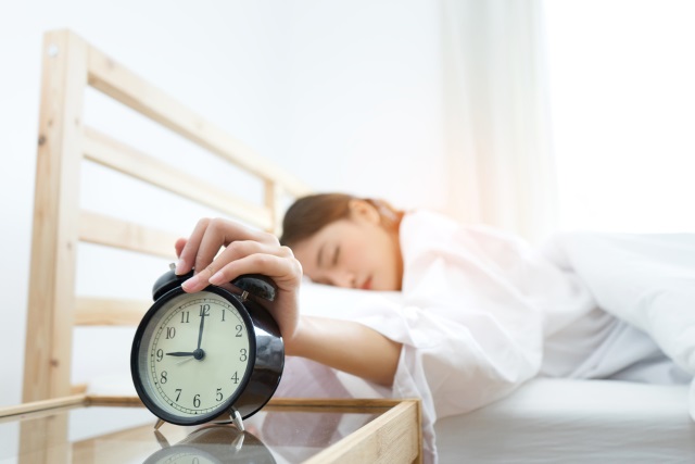 Women hitting snooze button on alarm clock