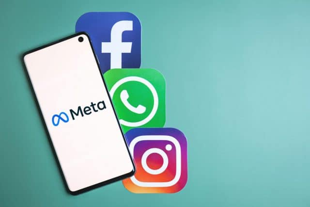 Meta logo on phone next to Facebook, Whatsapp and Instagram icons