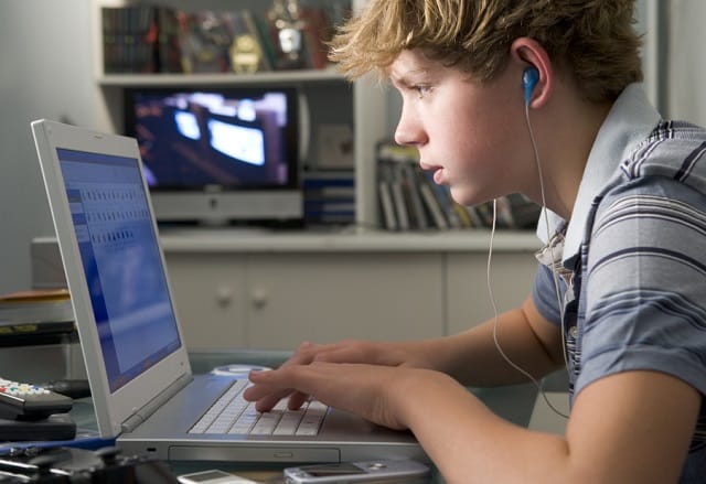Young boy in bedroom using laptop and listening to MP3 player