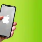 Hand holding an iPhone showing an Apple logo on a green background