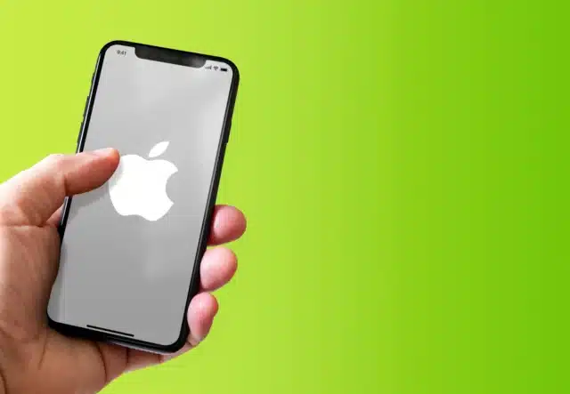 Hand holding an iPhone showing an Apple logo on a green background