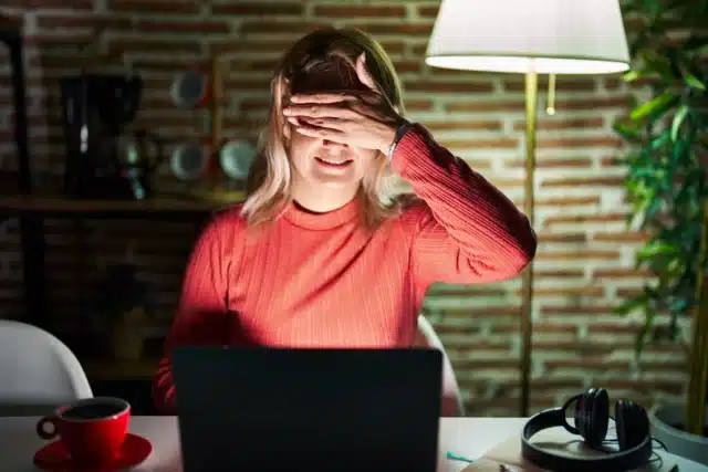 Woman at laptop hiding eyes