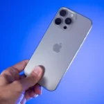 Blue background with a silver iPhone 16 being held in the middle